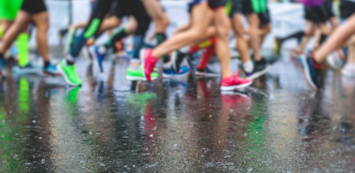 Marathon runners competition in the rain close-up, view of footwear running shoes during half-marathon on the city asphalt streets with water splashing, crowd of joggers in motion, outdoor training