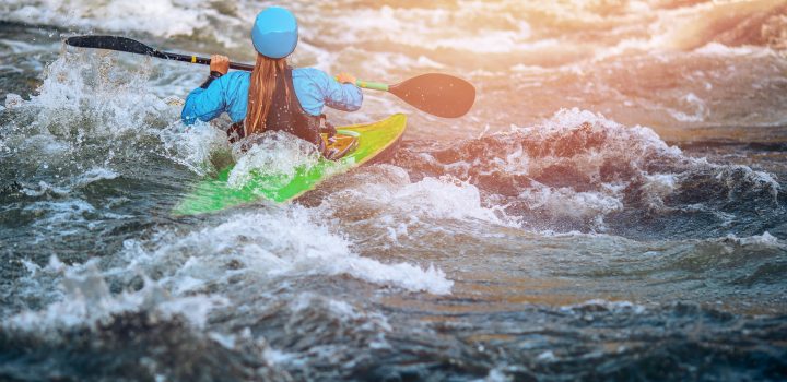 Girl in kayak sails mountain river. Whitewater kayaking, extreme sport rafting.
